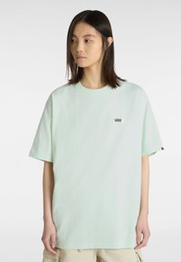 Mintgrünes oversized T-Shirt aus Baumwolle. Mit kleinem schwarzen Vans-Logo auf der linken Brust. Kurze Ärmel und runder Halsausschnitt.
