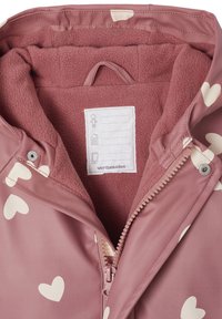 Pink jacket with large cream hearts, features a soft fleece lining, zipper closure, and a care label inside the collar area.