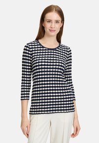 Gestreifte Langarmbluse in Marineblau und Creme mit rundem Halsausschnitt und strukturiertem Stoff, der wellenförmige horizontale Muster aufweist und eine figurbetonte Silhouette hat.