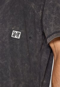 T-shirt noir à manches courtes en tissu texturé, présentant un motif légèrement décoloré. Comprend une étiquette avec le logo Nike blanc sur le côté supérieur gauche.