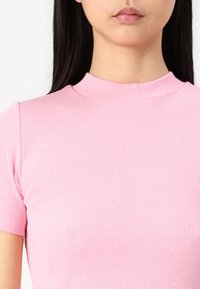 Rosa ribbad top med korta ärmar har en hög halsringning och en figurnära silhuett, som visar en mjuk textur och subtila vertikala linjer.