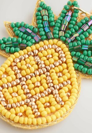 Accessoire en forme d'ananas en perles, présentant des perles jaunes, vertes et dorées, avec une surface texturée et des détails de design élaborés.