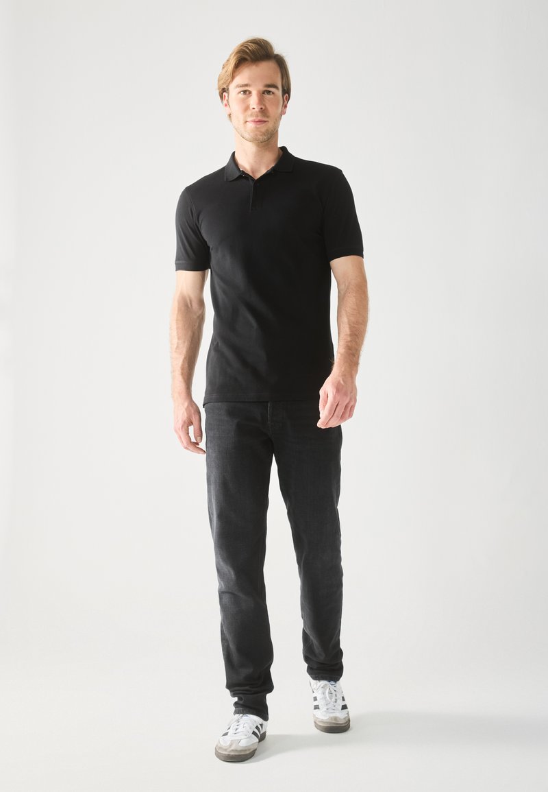 Sort kortærmet polo skjorte båret med mørke jeans og hvide sneakers. Klassisk design, glat tekstur og en diskret krave.