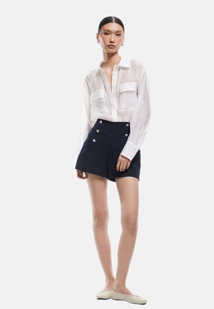Witte transparante lange mouw shirt met twee borstzakken, gecombineerd met marineblauwe high-waisted shorts met zilveren knopen. Glad materiaal.