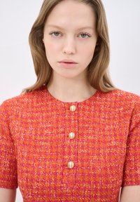Abito texture rosso e rosa con maniche corte, caratterizzato da un collo rotondo e tre bottoni dorati sul davanti.