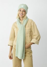 Mint green knitted beanie and matching scarf displayed against a light background. Scarf features a textured pattern and logo patch.