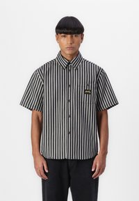 Black and white striped short-sleeve shirt with a button-up front, featuring a chest pocket and logo detail. Smooth fabric texture.