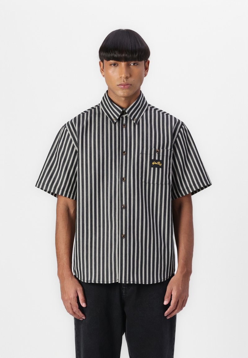 Black and white striped short-sleeve shirt with a button-up front, featuring a chest pocket and logo detail. Smooth fabric texture.
