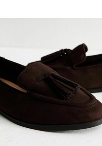 Mocasines de ante marrón con un frente con borlas, punta redondeada y suela baja de goma negra. Textura suave y diseño estructurado.