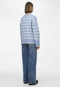 Ljusblå randig tröja med korta, breda ärmar, kombinerad med lösa blå jeans. Tröjan har en ribbad nederkant och ribbade manschetter.