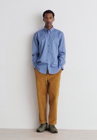 Camicia azzurra a righe con bottoni, pantaloni beige a gamba larga e calzature verdi. Design semplice con una vestibilità rilassata, senza motivi visibili.