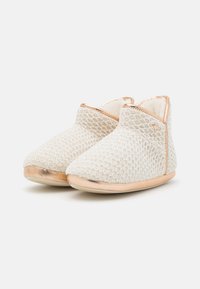 White woven slippers with a textured surface, rose gold accents, and a low profile. The sole is light and flexible, enhancing comfort.