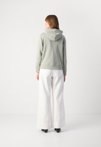 Felpa verde chiaro con una texture morbida, dotata di cappuccio e polsini a costine, abbinata a pantaloni bianchi a gamba larga e scarpe nere con tacco.