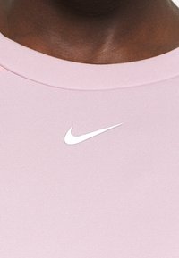T-shirt de sport rose clair avec une texture côtelée. Présente un petit logo blanc Nike sur la poitrine. L'encolure est arrondie.