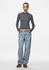 Námořnický pruhovaný žebrovaný top s dlouhým rukávem a zkráceným lemem, kombinovaný se světlými modrými volnými džíny a hnědými botami. Jednoduchý design a ležérní vzhled.