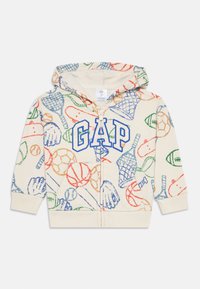 Felpa crema con logo "GAP" blu. Presenta stampe sportive colorate in rosso, verde e arancione. Zip intera, tasca a marsupio e cappuccio.