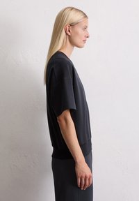 Zwarte korte mouw sweatshirt met een relaxte pasvorm, geribde zoom en zachte textuur, gedragen door een model tegen een neutrale achtergrond.