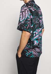 Chemise à manches courtes avec une base noire ornée de motifs de feuilles turquoise vif et lavande, coupe décontractée et col.