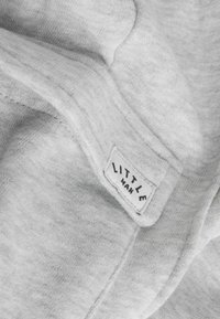 Grijze stof van een sweatshirt met een zachte textuur. Bevat een label met de tekst "LITTLE MAN" in zwarte letters op een witte achtergrond.