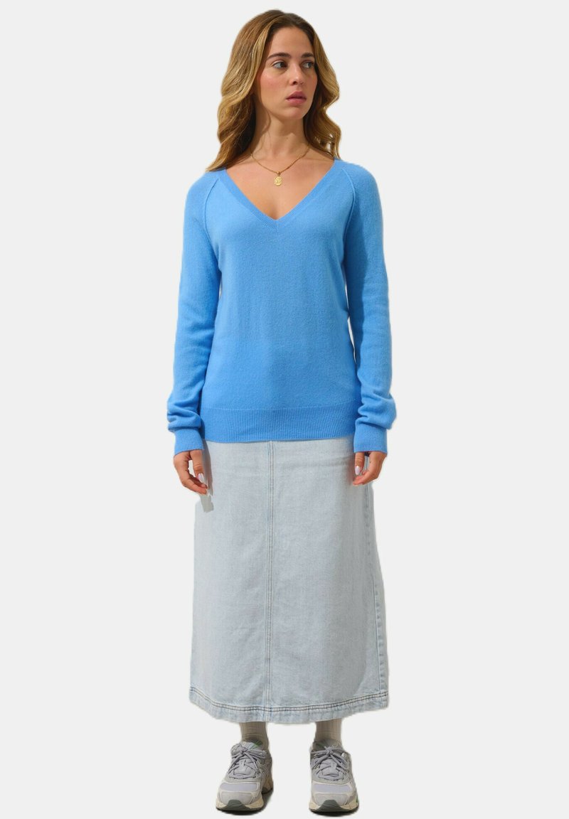 Ljusblå, V-ringad tröja med långa ärmar; ihop med en ljus denim maxikjol. Skorna är grå sneakers. Enkelt mönster och texturerad tyg.