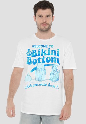 White cotton T-shirt featuring blue graphic text: "Welcome to Bikini Bottom" and cartoon images of a pineapple and a stone house.