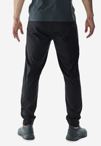 Pantalones deportivos negros hechos de un material ligero y elástico; puños ajustados y textura suave. Combinados con zapatillas deportivas grises.