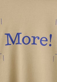 Tissu beige avec le mot « Plus ! » imprimé en grandes lettres bleues centré dessus.