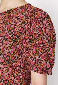 Blusa floral com um fundo preto e flores em tons de rosa, laranja e amarelo. As mangas bufantes e a textura plissada realçam o design.