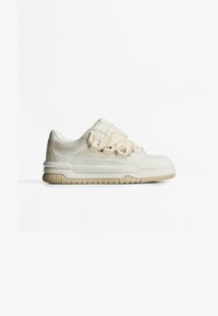 Lichtbeige sportshoe met mesh en synthetische materialen, dikke textuurzool en eenvoudig vetersysteem. Platte, afgeronde neus, minimale accenten.