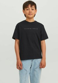 Juoda medvilninė marškinė su trumpomis rankovėmis, ant krūtinės esantis baltas "JACK & JONES" užrašas, derinamas su šviesiai mėlynomis džinsinėmis kelnėmis.