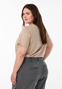 Beige T-Shirt mit kurzen Ärmeln, kombiniert mit grauen, gestreiften Hosen. Die Hosen haben eine glatte Textur und eine taillierte Passform mit Gesäßtaschen.