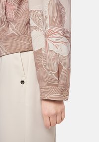 Floral-patterned, sheer fabric jacket in muted pink tones. Features a button accent on the sleeve. Smooth texture and relaxed fit.