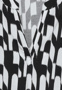 Camicia bianca e nera caratterizzata da un potente motivo astratto, con scollatura a V e un dettaglio decorativo con bottoni al colletto.