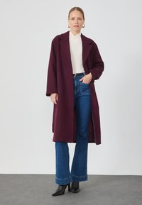 Cappotto lungo e aperto davanti in lana borgogna, con colletto revers e maniche oversize. Abbinato a jeans a gamba larga blu e stivali neri con punta.
