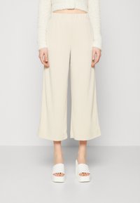 Beige wijde broek met een elastische tailleband, gemaakt van een zacht materiaal. Gecombineerd met chunky witte platform sandalen.