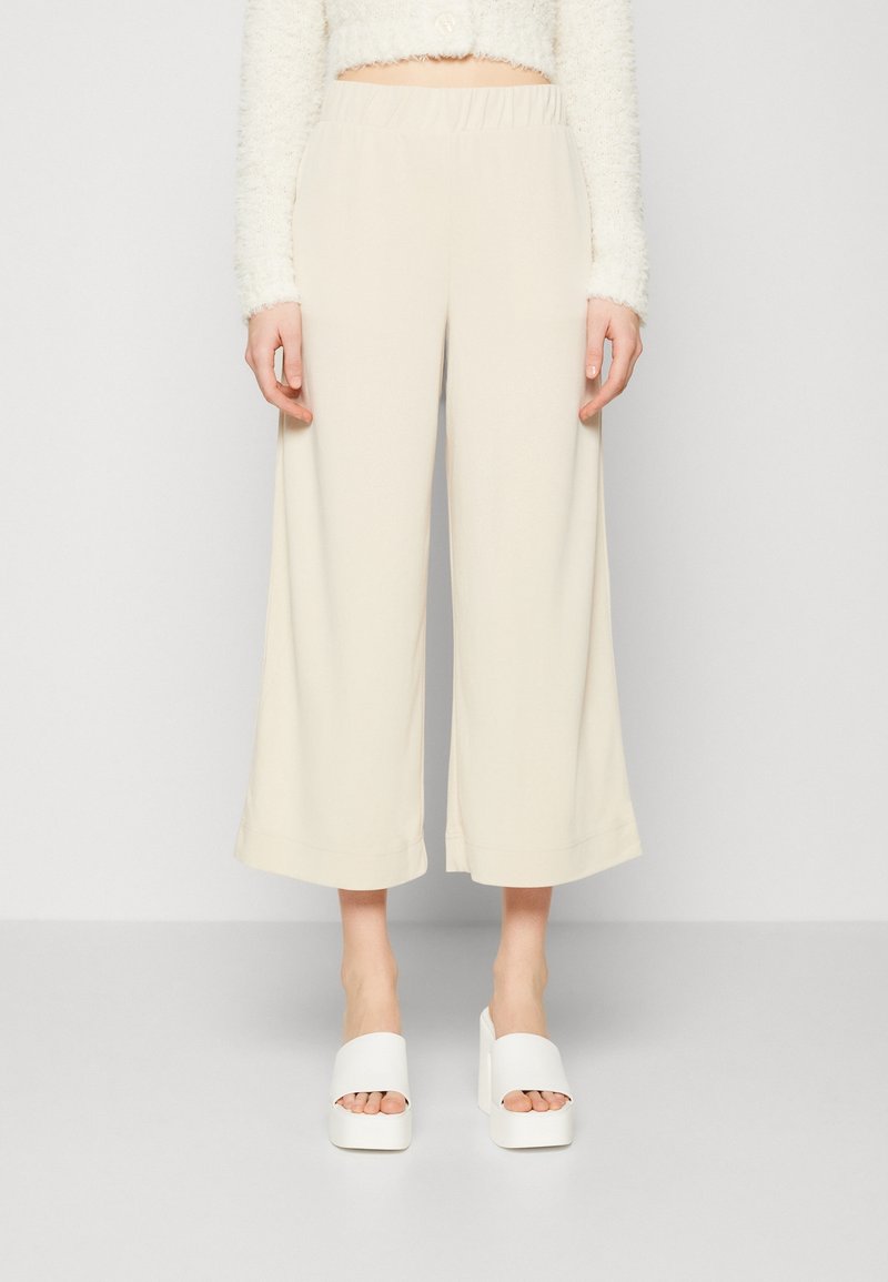 Beige wijde broek met een elastische tailleband, gemaakt van een zacht materiaal. Gecombineerd met chunky witte platform sandalen.