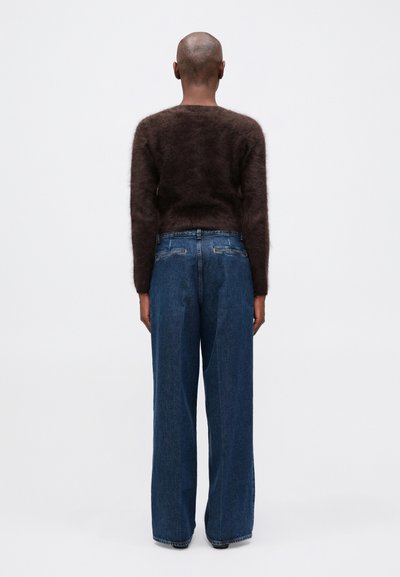 Suéter marrón de mohair con una textura suave, combinado con jeans de pierna ancha azules. El conjunto se observa desde la parte trasera contra un fondo liso.