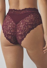 Woman wearing burgundy lace high-waist underwear, showing detailed floral lace pattern and scalloped edges from the back.
