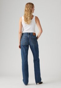 Blauwe spijkerbroek met uitlopende pijpen, een middelhoge taille en achterzakken. De stof heeft een klassieke textuur en komt tot de enkel.