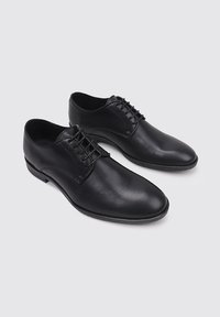 Zapatos de cuero negro con cordones, acabado suave, puntera redondeada y detalle de costura en contraste en la parte superior. Suela de goma duradera.