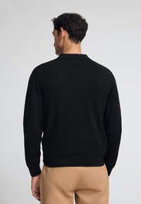 Svart knittrande tröja med krage och ribbade ärmslut. Mjuk textur, skräddarsydd passform och en enkel baksida utan dekorationer.