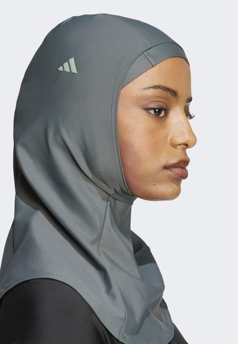 Grauer Sports-Hijab aus glattem, dehnbarem Stoff. Hat ein elegantes Design mit einem minimalistischen Logo und nahtlosen Kanten. Sitzt eng an.