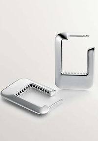 Pendientes de metal plateado con un diseño geométrico rectangular abierto. Superficie lisa, acabado pulido y borde interior texturizado.