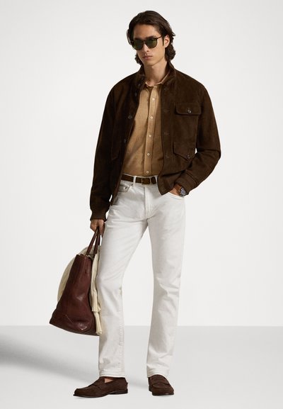 Brązowa zamszowa kurtka, jasno-brązowa koszula zapinana na guziki, białe jeansy, brązowy pasek, brązowe mokasyny i okulary przeciwsłoneczne. Trzyma brązową torbę typu tote z kremowym akcentem.