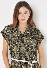 Abito camicia verde con motivo, maniche corte, caratterizzato da design floreali e geometrici; vita legata con una cintura di corda, apertura con bottoni.