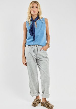 Top en denim sans manche bleu clair avec un décolleté en clé, pantalon gris confortable, et sabots imprimé léopard. Écharpe nouée autour du cou.