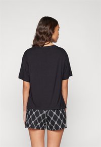 T-shirt noir à coupe décontractée et manches courtes, associé à un short noir avec un motif de chaîne géométrique blanche.