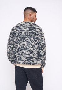 Übergroßer, gestrickter Pullover mit grau-weißer Wirbelmuster. Weiche, fuzzy Textur mit einem cremefarbenen Saum. Lässige Passform mit abgesenkten Schultern.