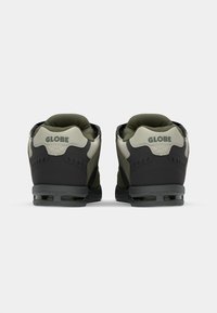 Black and olive green sneaker featuring a smooth leather and mesh upper, cushioned heel, and visible air cushioning in the sole.