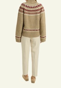 Beige gestrickter Pullover mit hohem Kragen, versehen mit einem Muster aus roten und cremigen geometrischen Akzenten, kombiniert mit hellbeigen Hosen und Holzclogs.